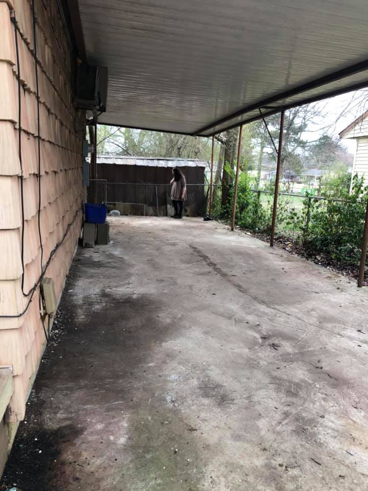 A person is standing in a parking lot under a carport.