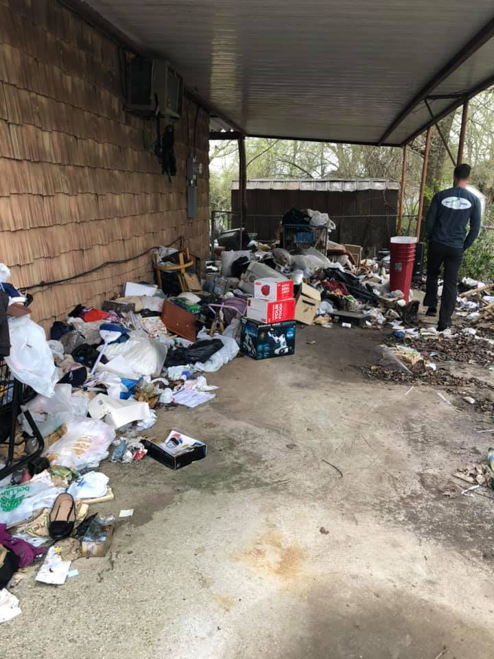 A man is standing in front of a house that is covered in trash.