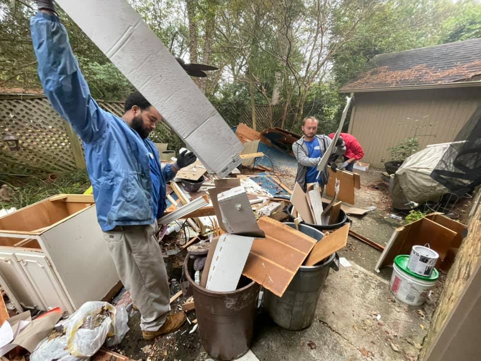 A man is standing in a pile of trash holding a piece of wood.