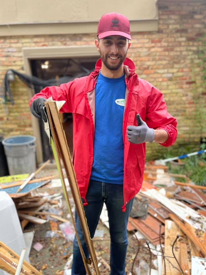 A man in a red jacket is holding a piece of wood and giving a thumbs up.