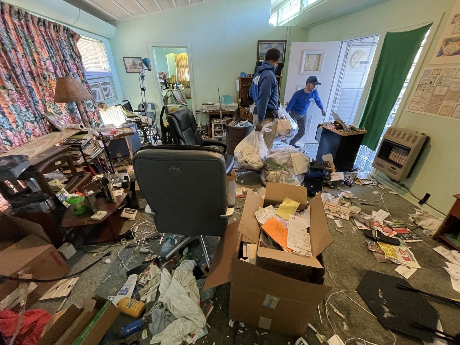 A man is standing in a messy room with boxes on the floor.