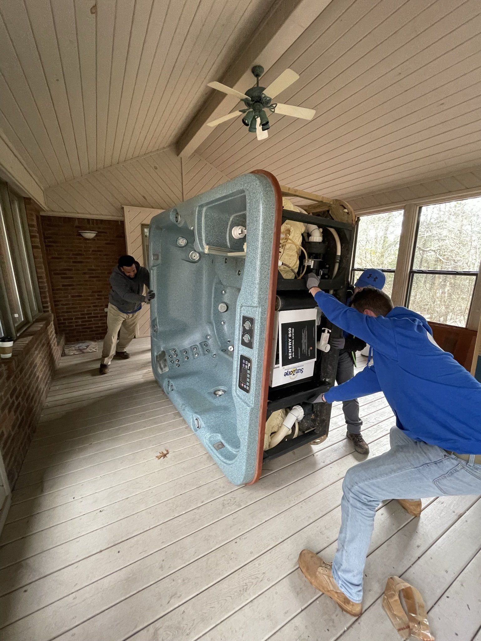 Two men are carrying a hot tub on a porch.