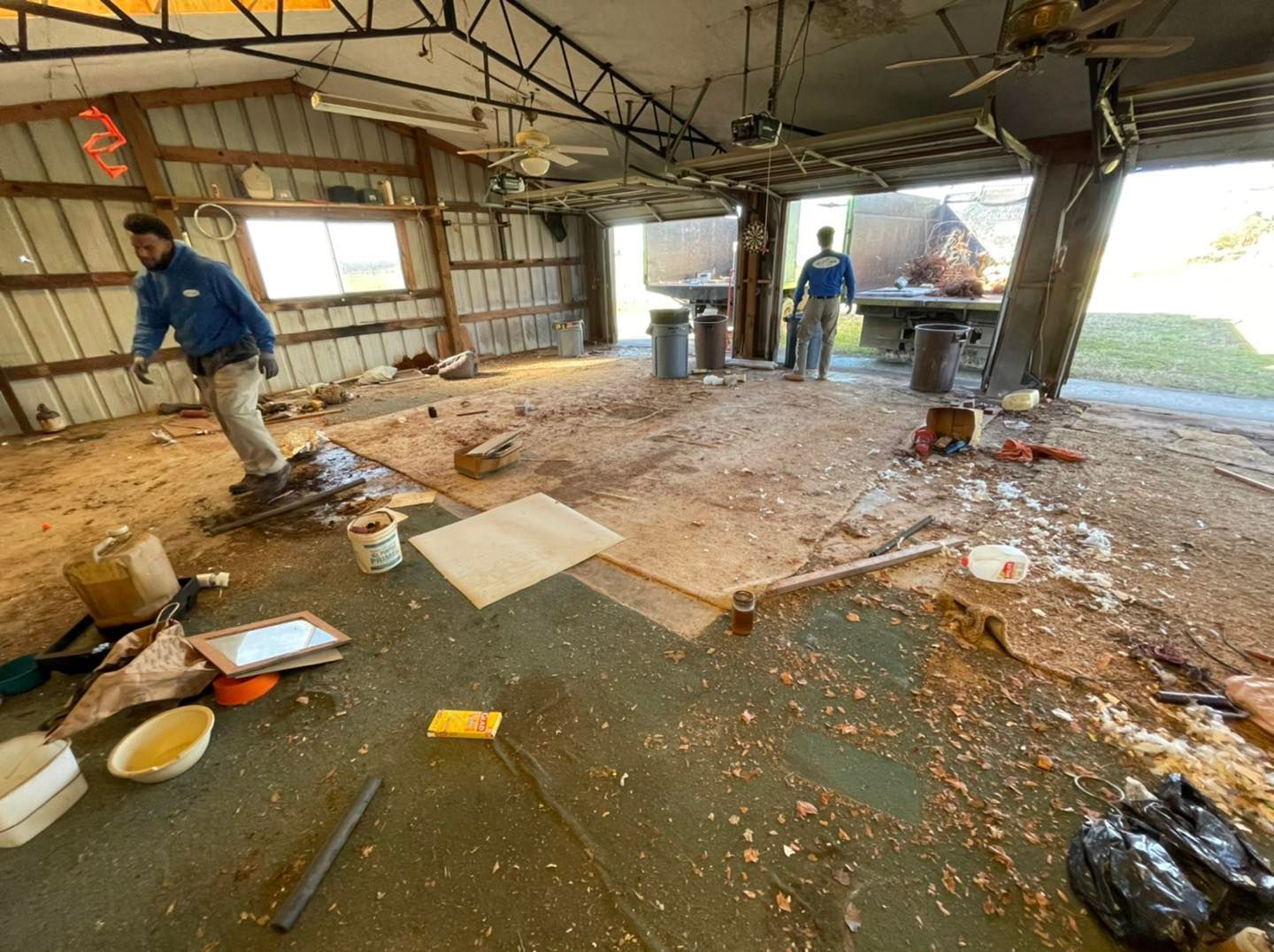 A man is standing in a messy room in a garage.