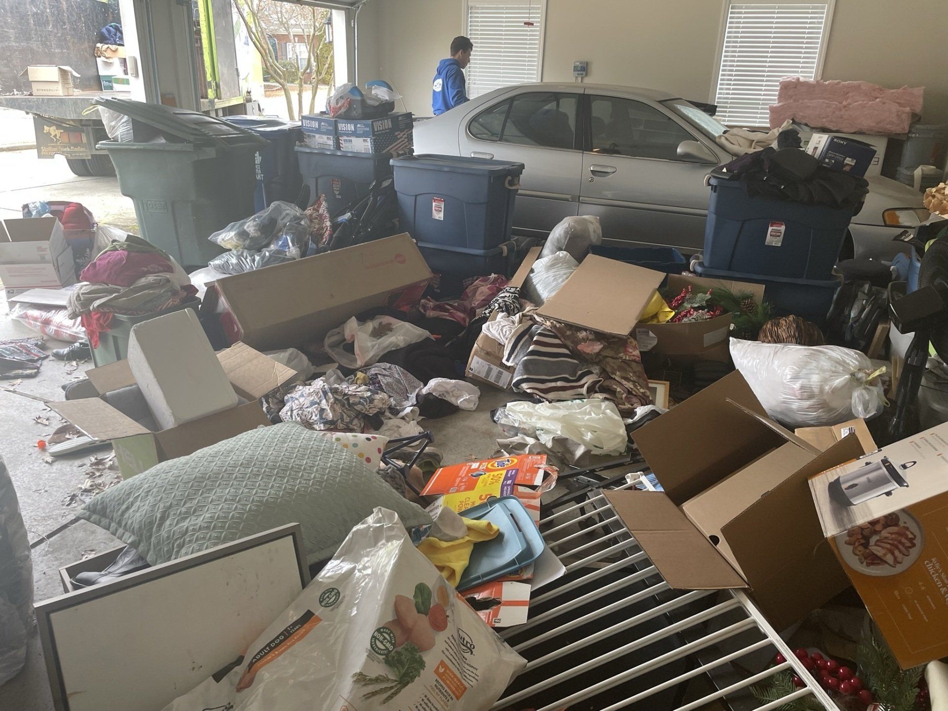 A car is parked in a garage filled with boxes and trash.