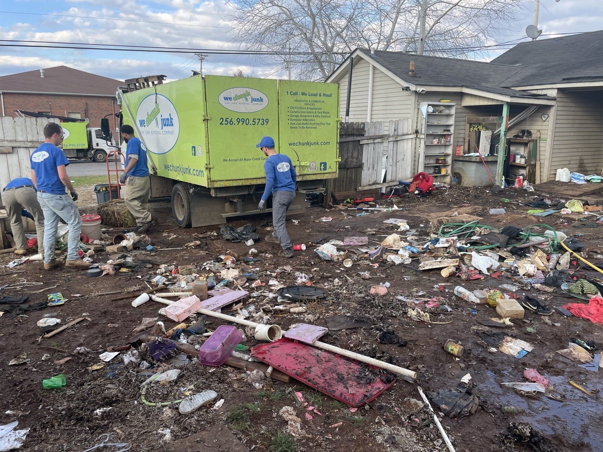 A group of men are cleaning a messy yard in front of a house.
