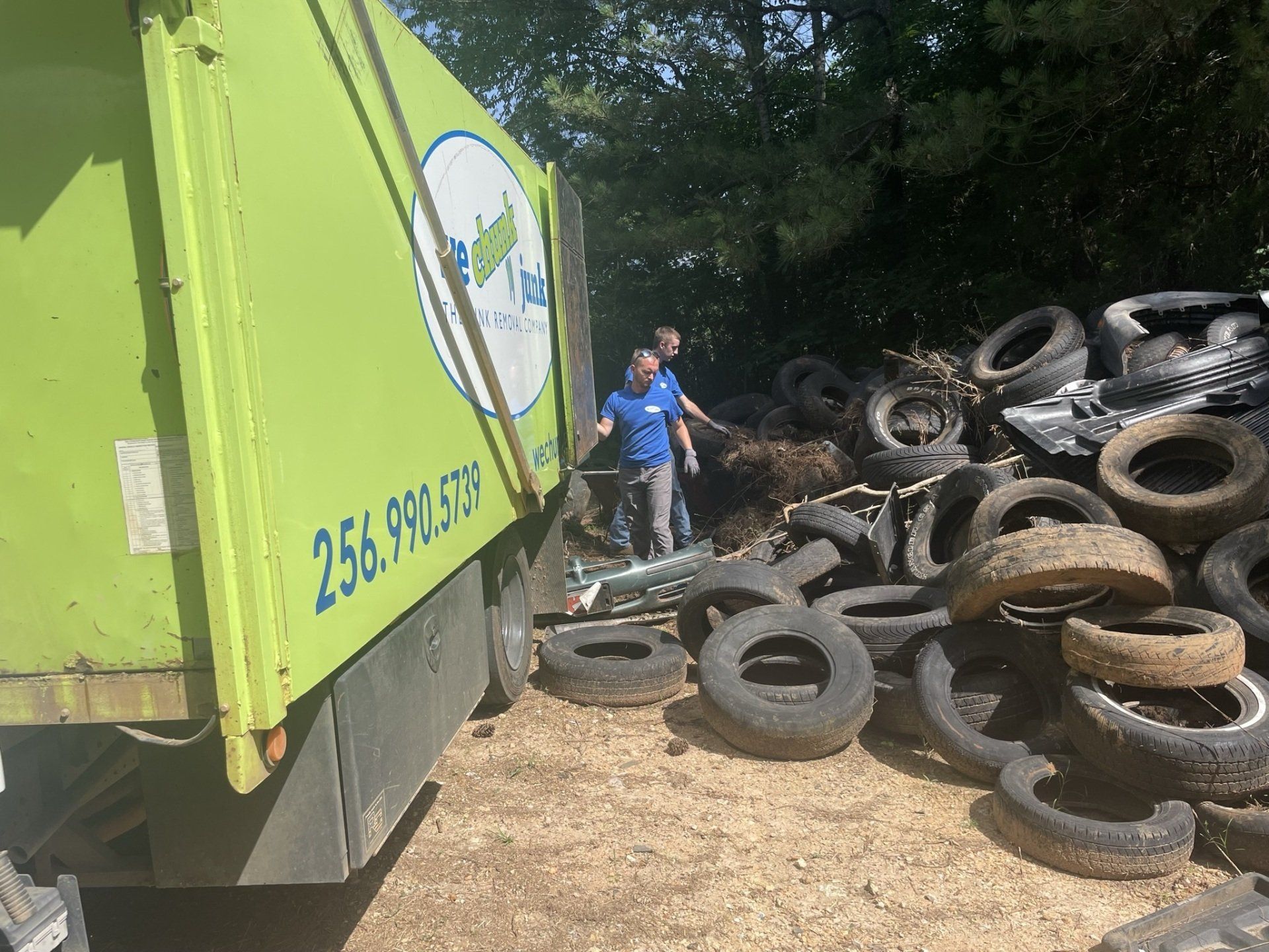 A green dumpster is sitting next to a pile of tires.