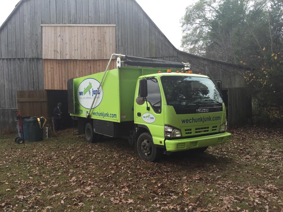 A green and white truck is parked in front of a barn.
