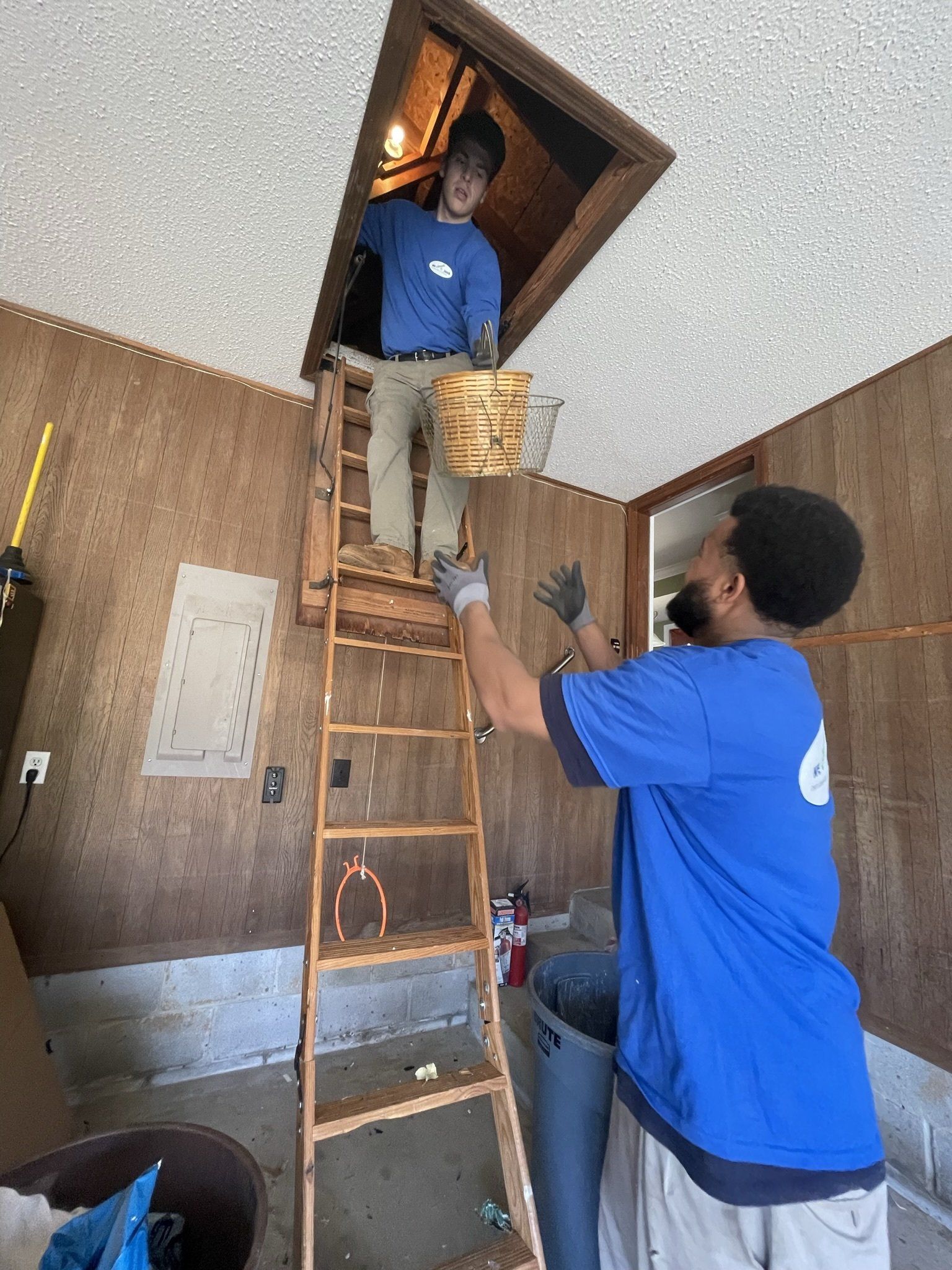 Two men are working on a ladder in a room.
