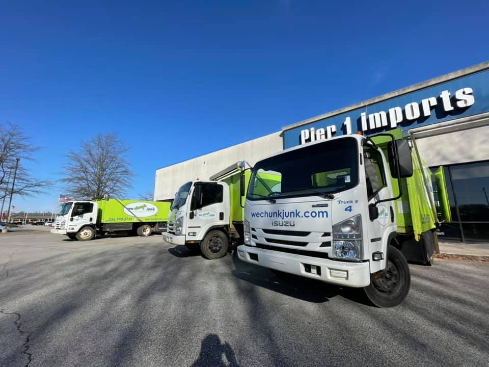 Three garbage trucks are parked in front of a pier 1 imports building.