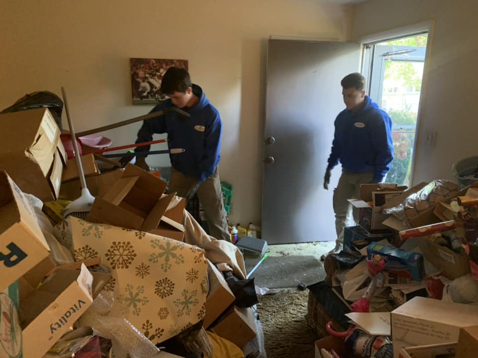 Two men are standing in a room filled with boxes.