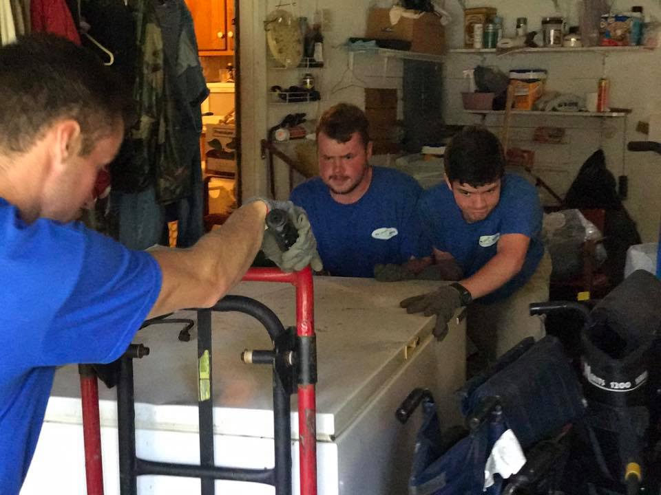 Three men in blue shirts are working on a freezer