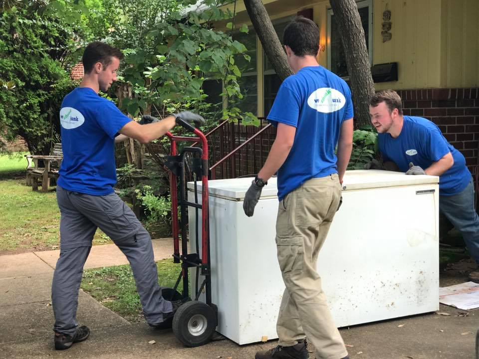 Three men in blue shirts are moving a freezer on a dolly.