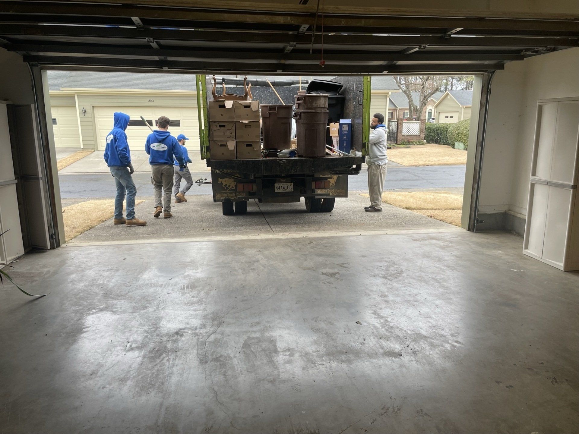 A group of people are standing in a garage next to a truck filled with boxes.