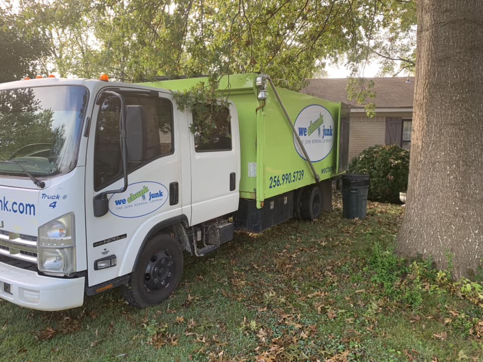 A green and white garbage truck is parked in front of a house.