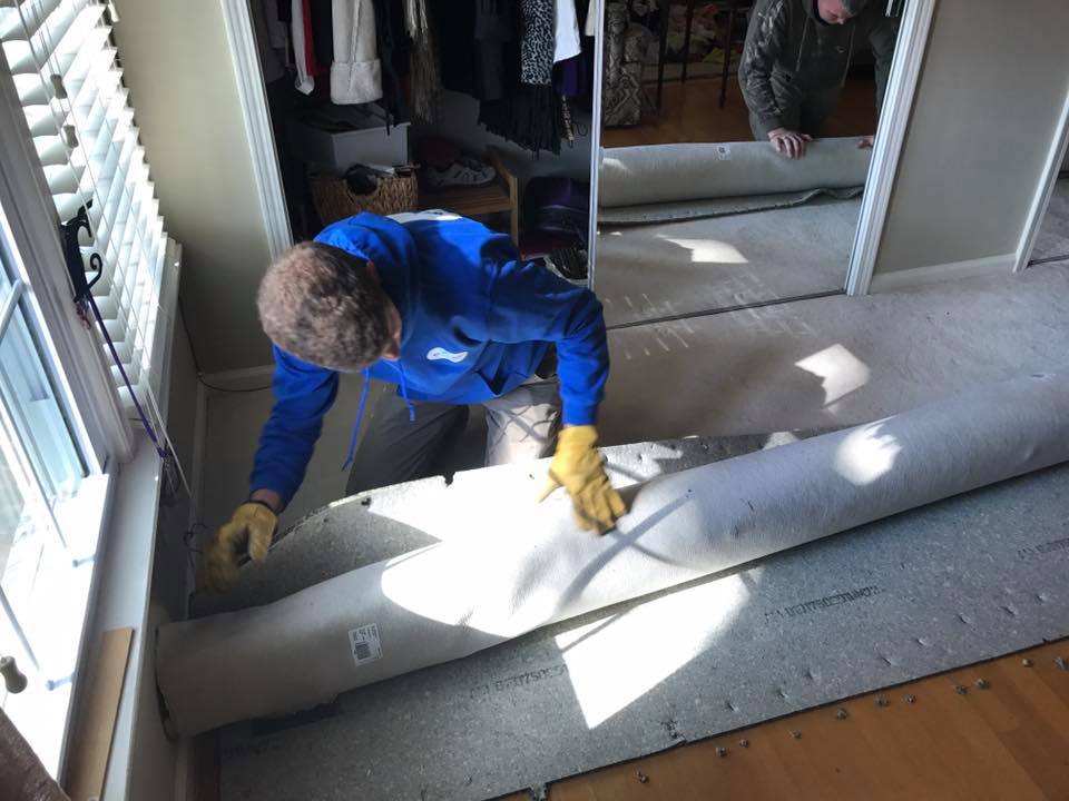 A man in a blue jacket is rolling a carpet in a room.