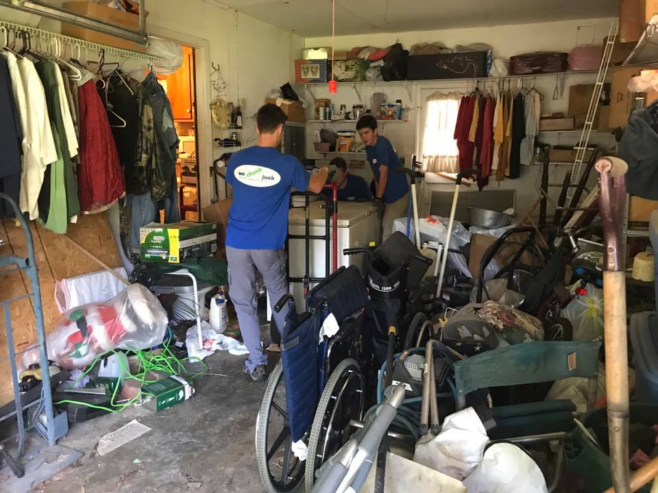 A man is standing in a garage filled with wheelchairs and clothes.