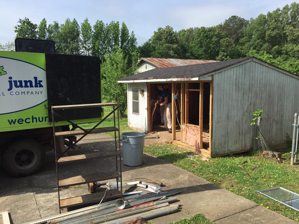 A junk truck is parked in front of a shed.
