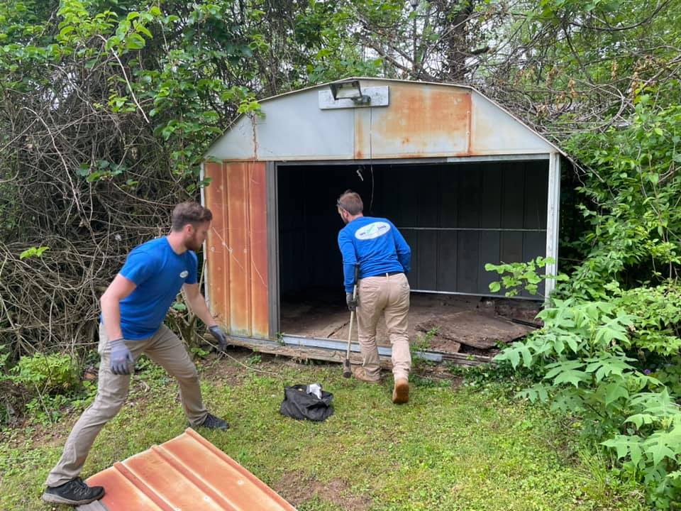 Two men are working on a shed in the woods.