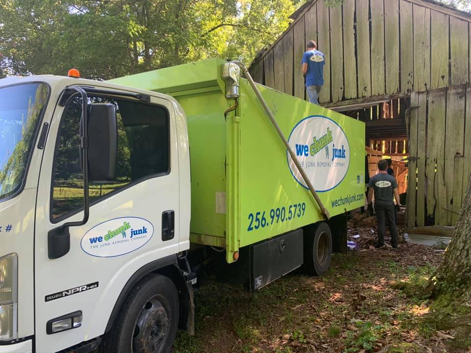 A green and white truck is parked in front of a wooden barn.