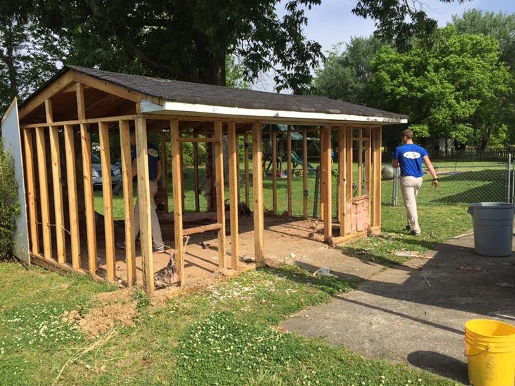 A man in a blue shirt is standing in front of a shed that is being built.