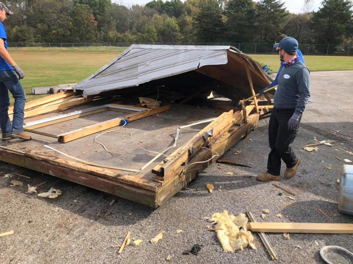 Two men are standing next to a wooden structure that has been damaged by a tornado.