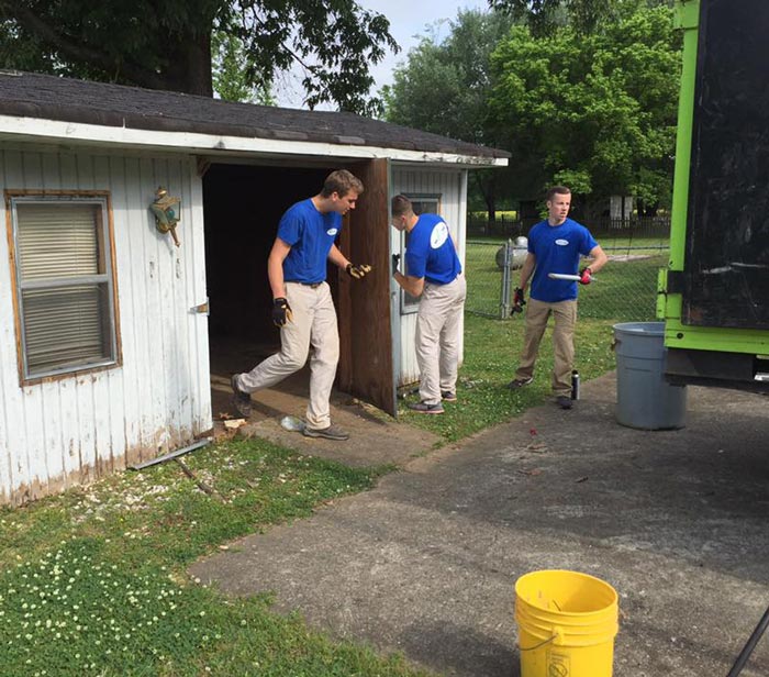 Three men in blue shirts are standing in front of a shed.