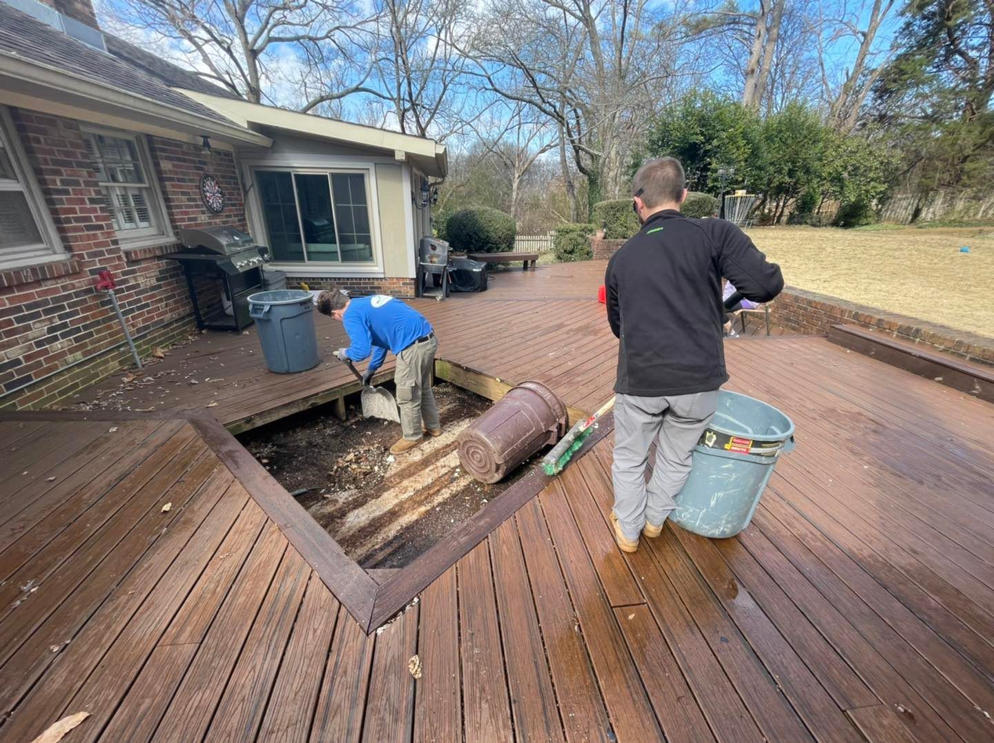 Two men are working on a wooden deck in front of a house.