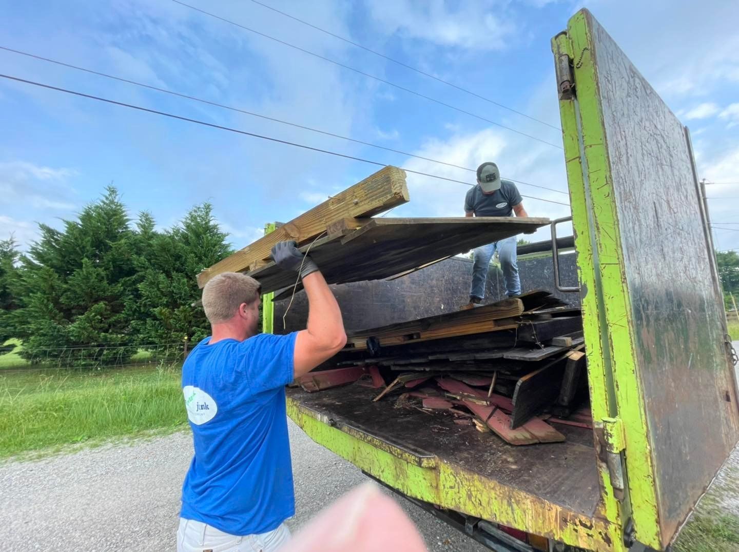 A man in a blue shirt is loading wood into a dumpster.