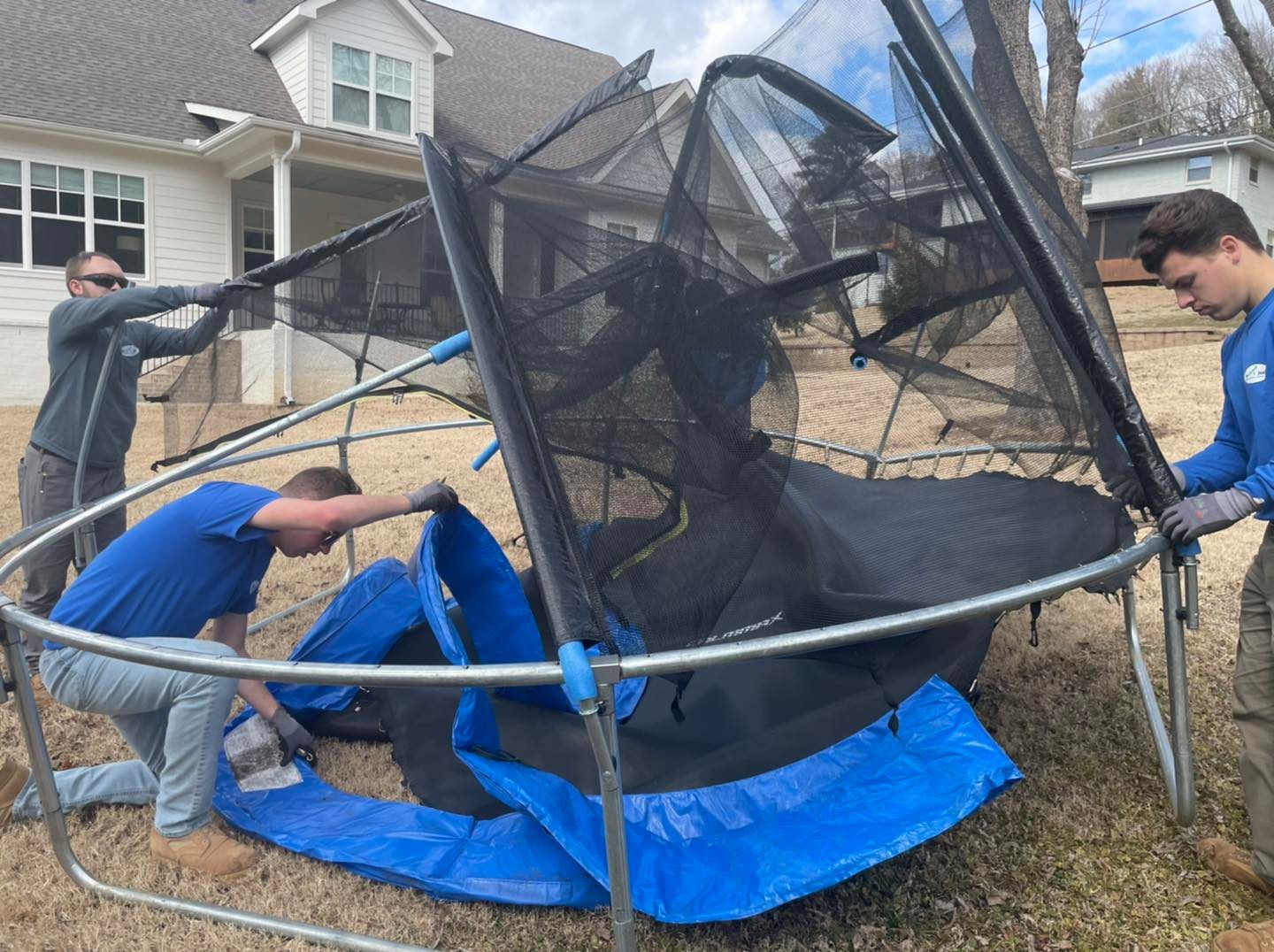 A group of men are working on a trampoline in front of a house.