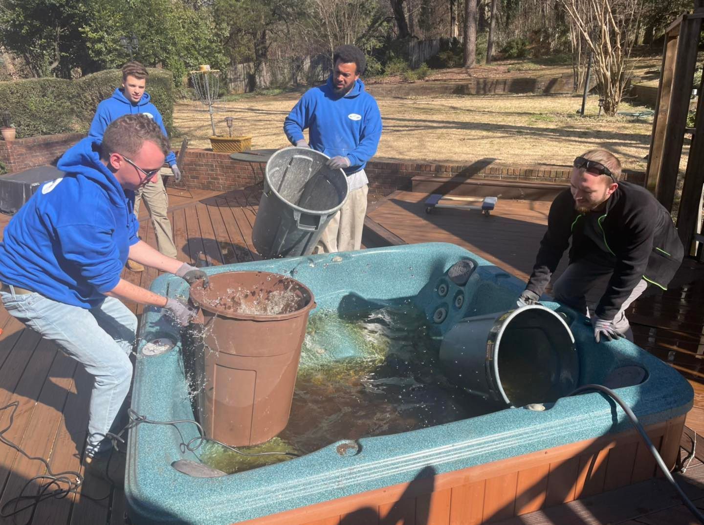 A group of men are cleaning a hot tub with buckets.