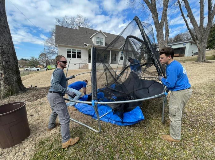 Two men are working on a trampoline in front of a house.
