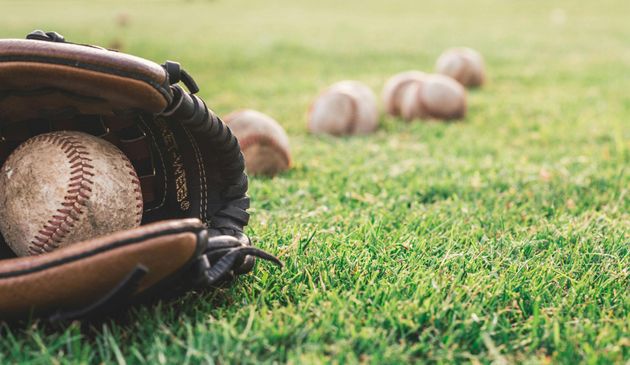 Baseball glove with ball on green grass, with blurred baseballs in the background.