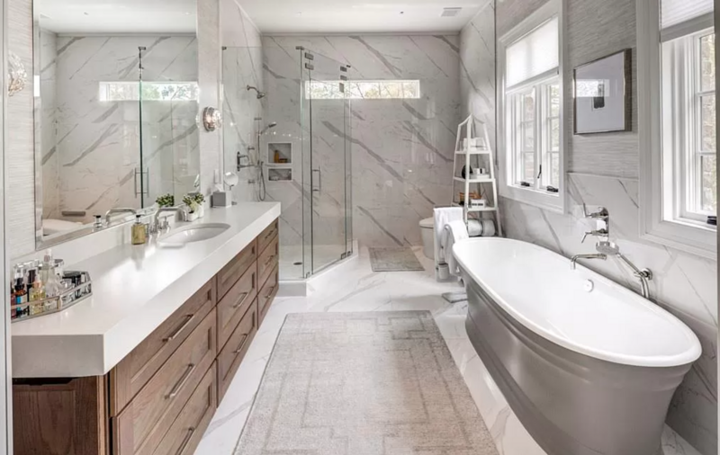 Spacious, modern bathroom with a white marble wall, double vanity, and a freestanding tub.