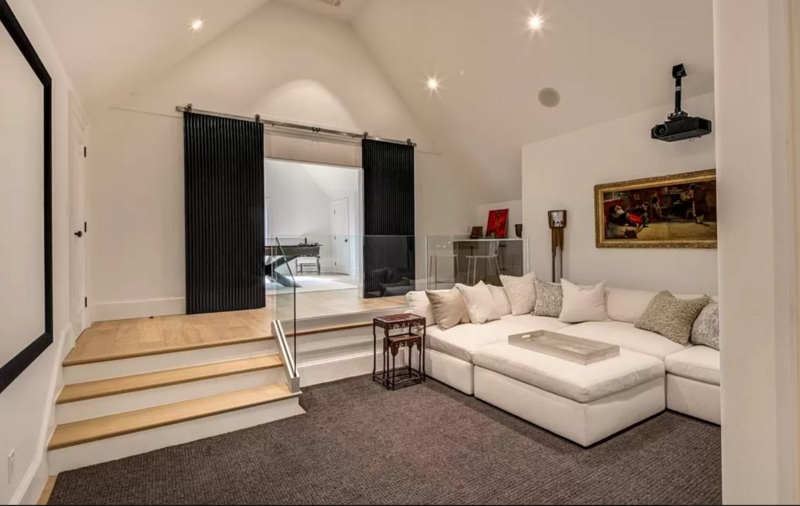 Home theater room with white sectional, steps, black sliding doors, and projector.