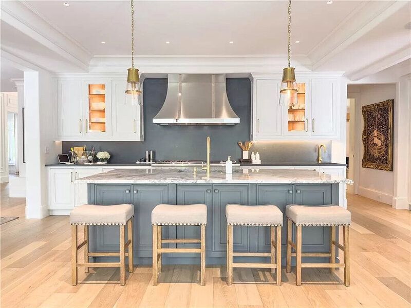 Elegant kitchen with blue island and white cabinets. Four bar stools, gold lighting, and stainless steel vent hood.