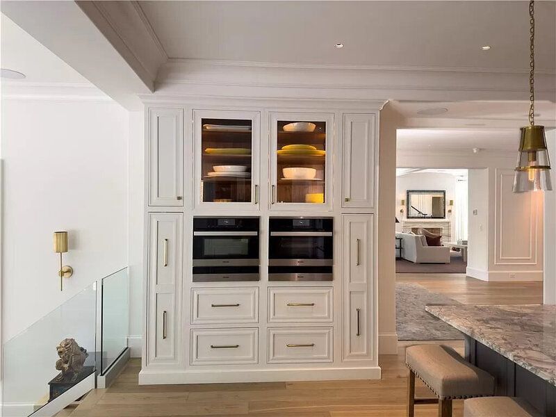 White built-in kitchen cabinets with microwave, ovens, drawers, and glass-door upper cabinets; a hallway is visible.
