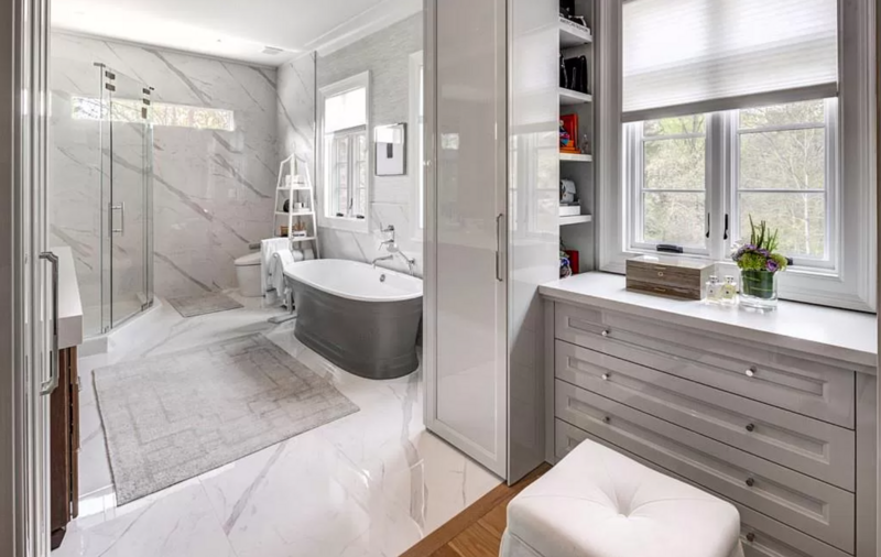 Luxurious white marble bathroom with a gray bathtub, vanity, and window seat.