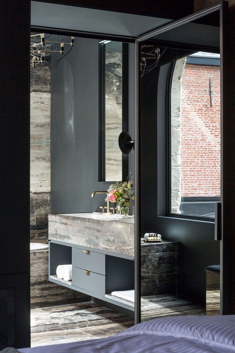 Dark gray bathroom with marble vanity, mirror, and tall window to brick building.