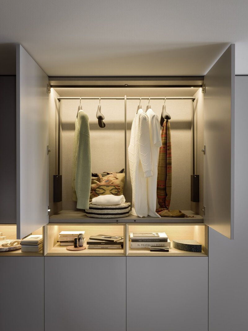 Built-in closet with hanging clothes, a shelf with books, and overhead lighting.