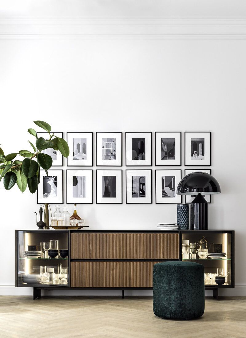 A modern living room with a credenza, photo frames, a lamp, and a green ottoman.