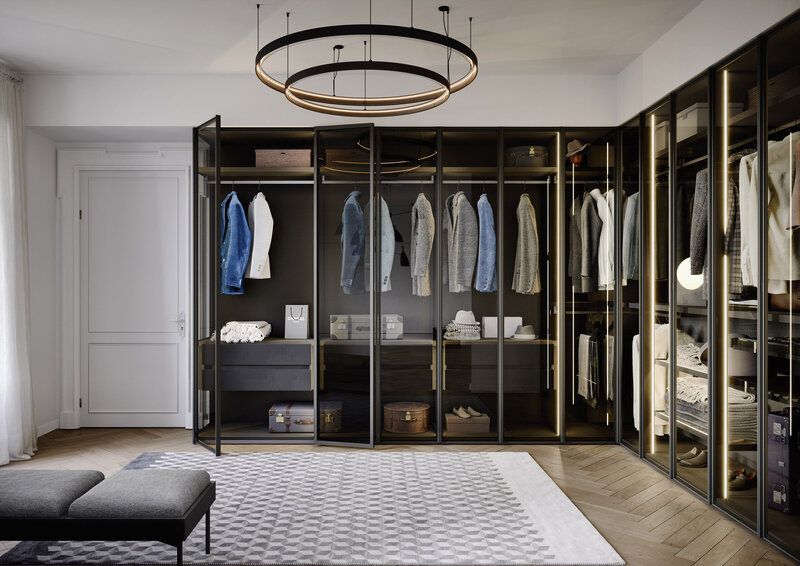 Walk-in closet with dark framed glass doors, filled with hanging clothes, drawers, and shelving. A modern light fixture hangs overhead.