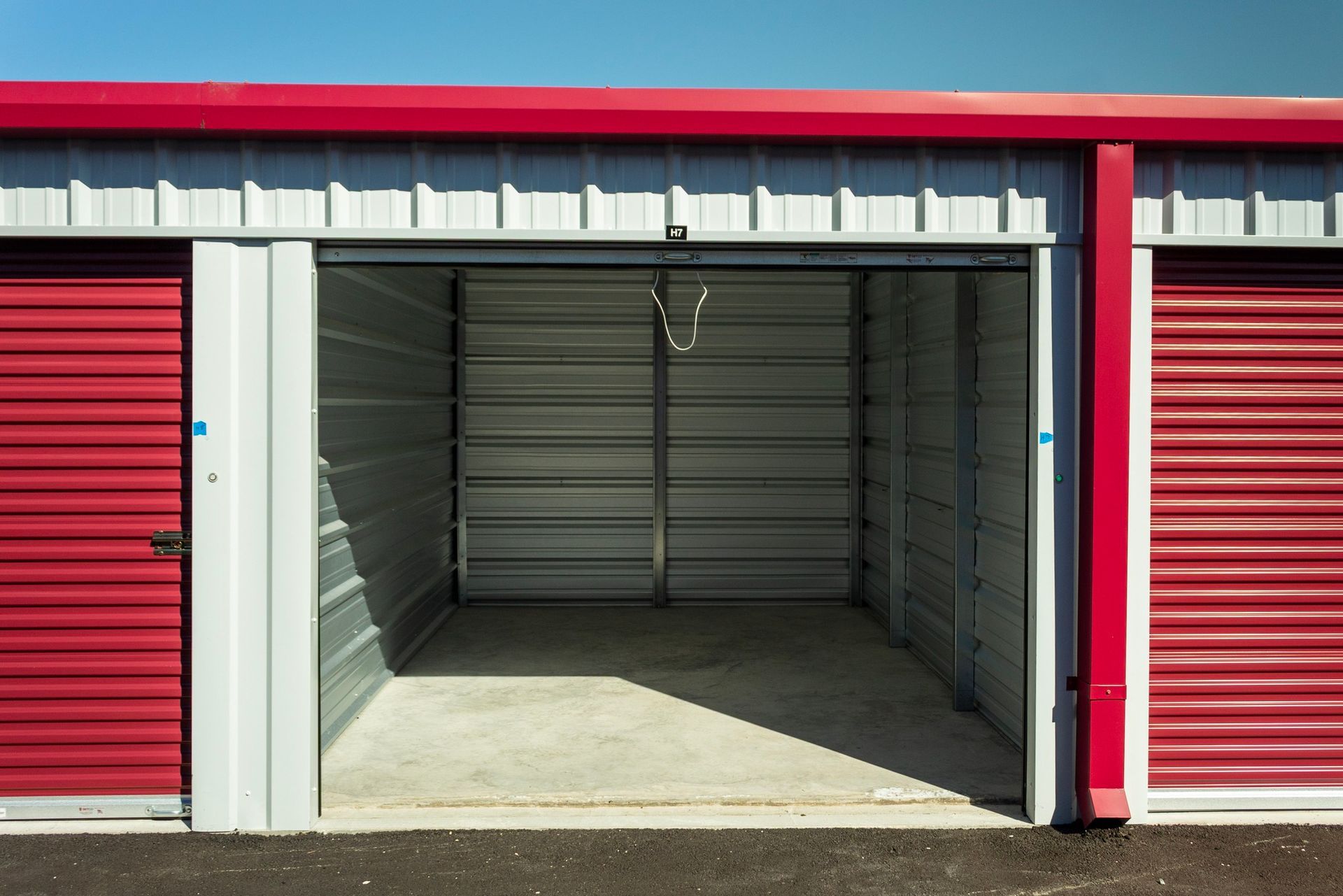 Storage unit, open doorway, red doors, metal siding, concrete floor.