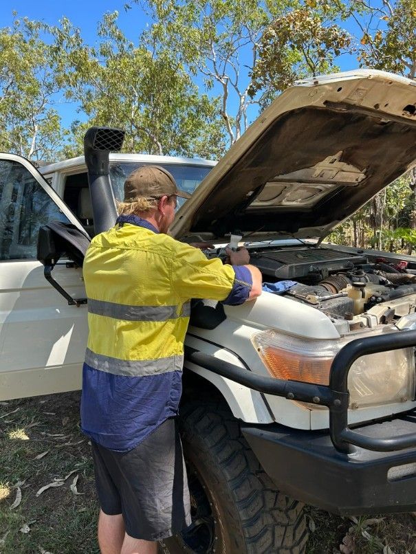 Man in High-vis Shirt Working on a White Vehicle With Open Hood Outdoors — Mudpig Mechanical In Humpty Doo, NT
