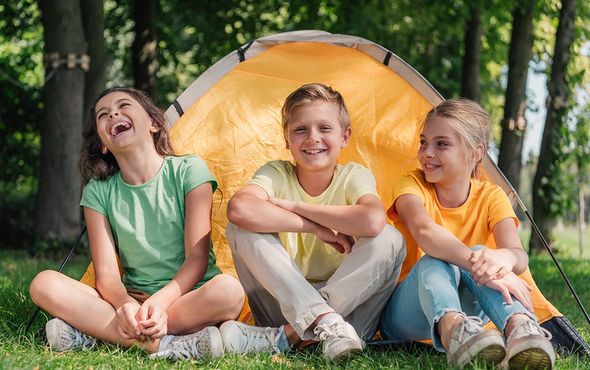 three children sitting in front of a yellow tent