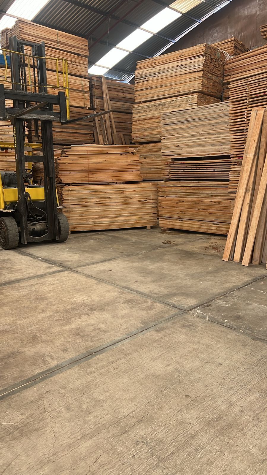 Una carretilla elevadora está moviendo paletas de madera en un almacén.