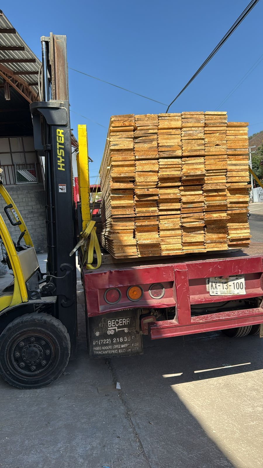 Una carretilla elevadora transporta una pila de madera en la parte trasera de un camión.