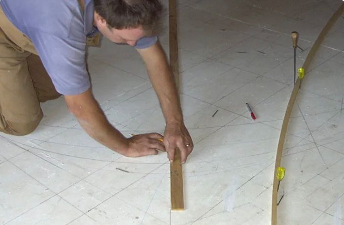 A man is measuring a piece of wood on the floor with a ruler.