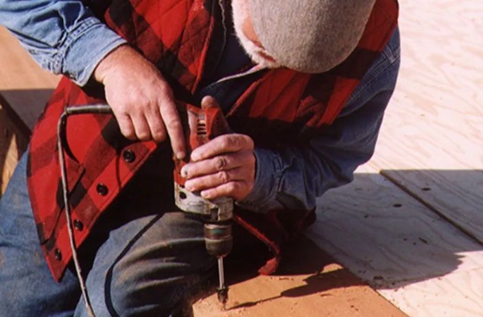 A man is using a drill to drill a hole in a piece of wood.