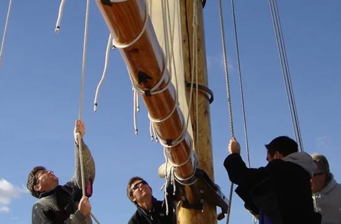 A group of people are working on a sailboat mast.