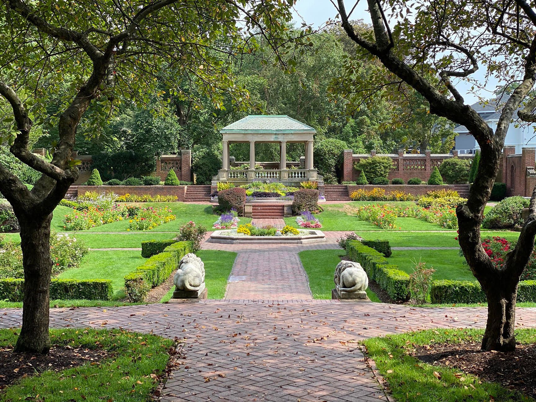 There is a gazebo in the middle of a garden surrounded by trees.